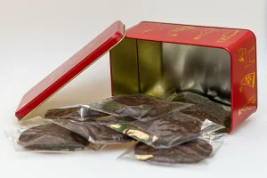 Blechtruhe in rot mit weichnachtlichem Motiv davor liegen Schokolebkuchen